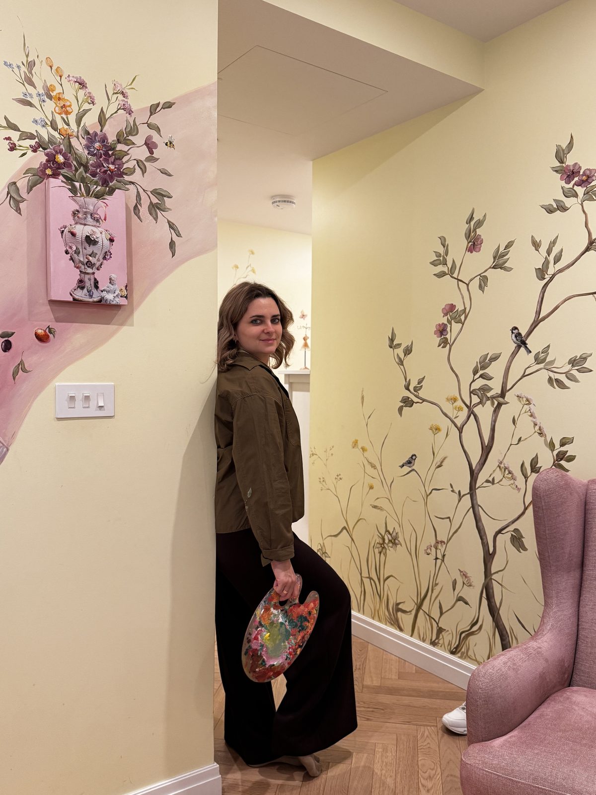 Bohdana Boikiv with her palette beside a hand-painted wall