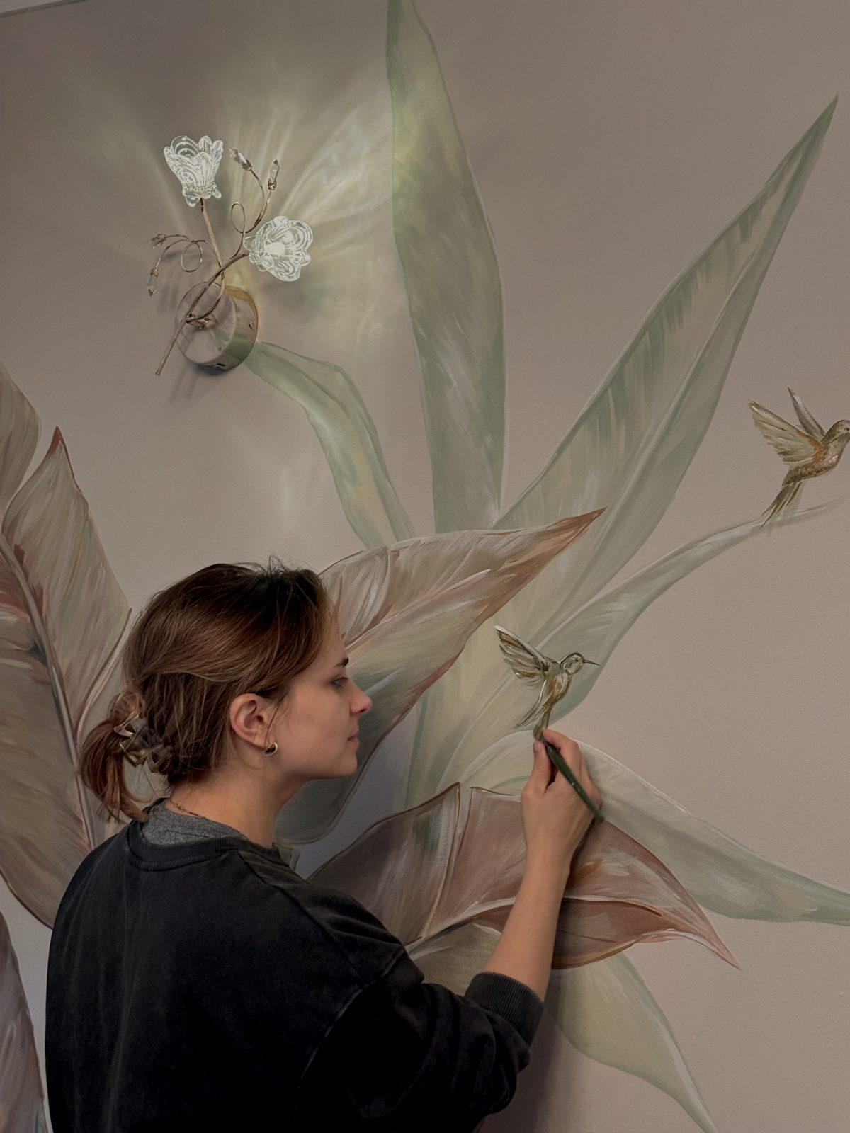 Bohdana painting a tropical leaves mural